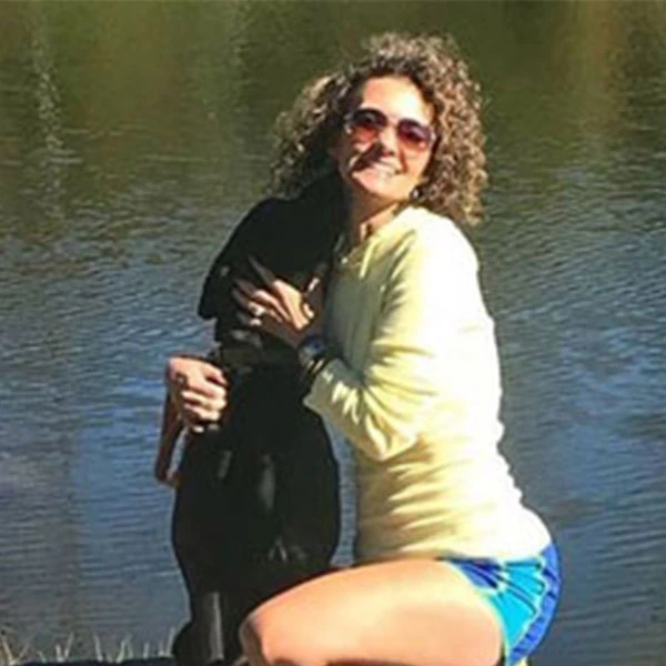 Jennifer hugging a black dog beside the water