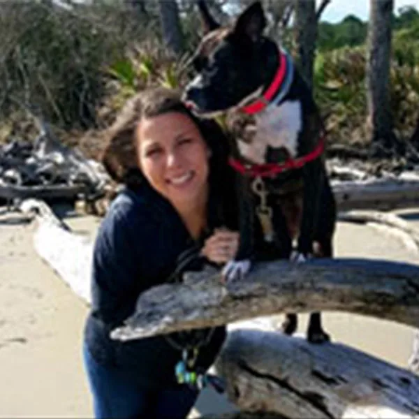 Megan with a black and white dog standing on driftwood on a beach
